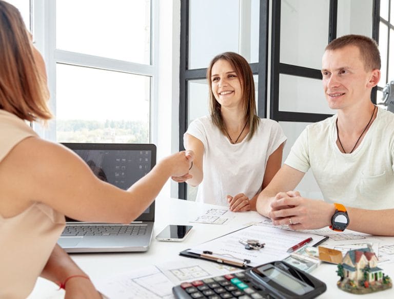Happy couple shaking hands with agent to finalize owner financing deal