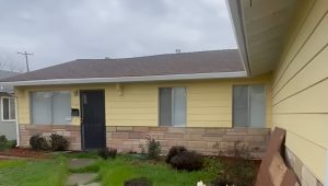 Yellow single-story home with worn exterior and overgrown front yard