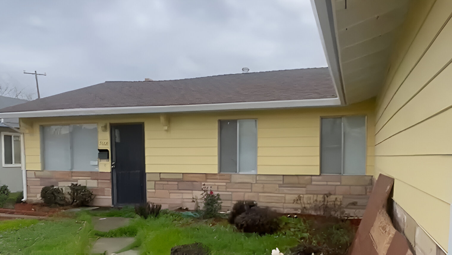 Yellow single-story home with worn exterior and overgrown front yard