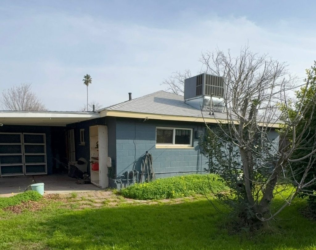 Backyard view of single-story home with garage and lawn for sale