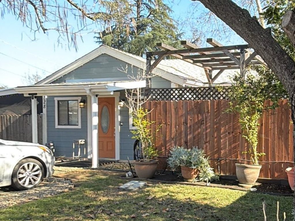Small single-family home with fenced yard, potted plants, and driveway parking